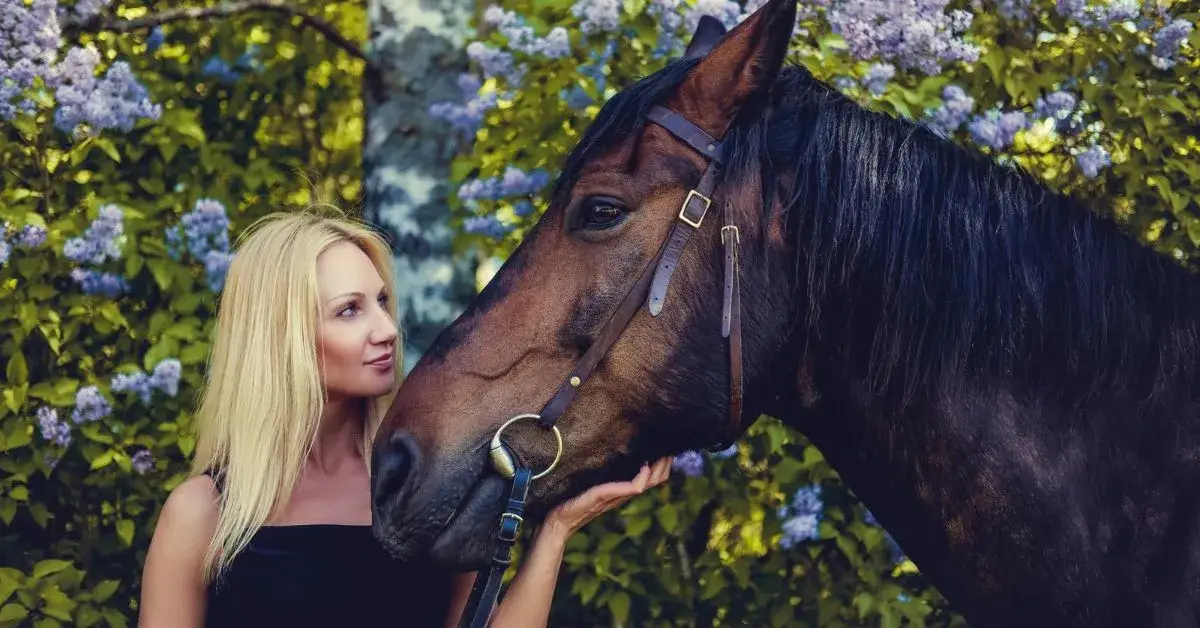 Beautiful woman bonding with a brown horse in a flower-filled garden
